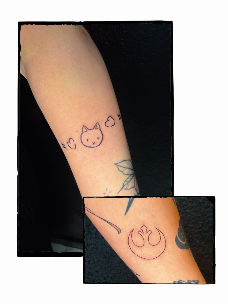 A minimalist black linework tattoo on the forearm featuring a cat face with hearts and a symbol — by Kiera Garvin, los angeles