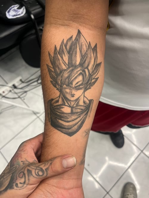 A black and grey anime-style portrait of Goku on the forearm, featuring detailed linework and shading — by Mr._Folks, los angeles