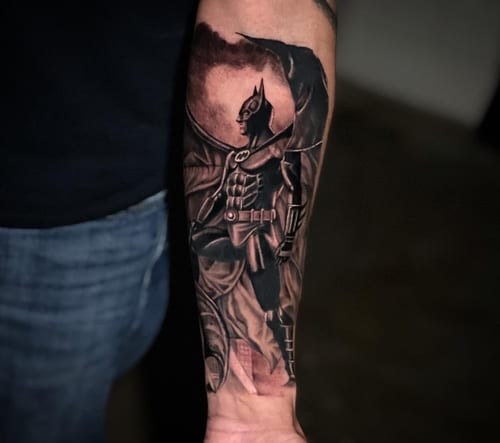 A detailed black and grey realism tattoo of Batman on the forearm, featuring intricate shading and a dramatic pose — by Travis Ross, los angeles