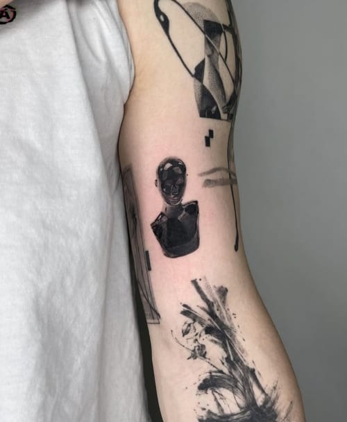 An abstract black and grey tattoo on the upper arm featuring a stylized face and geometric elements with bold blackwork and illustrative style — by Level tattoo, los angeles