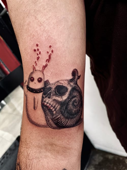 A mixed color and black and grey illustrative tattoo on the forearm, featuring a whimsical creature next to a skull with a snake wrapped around it — by zitronxus, los angeles