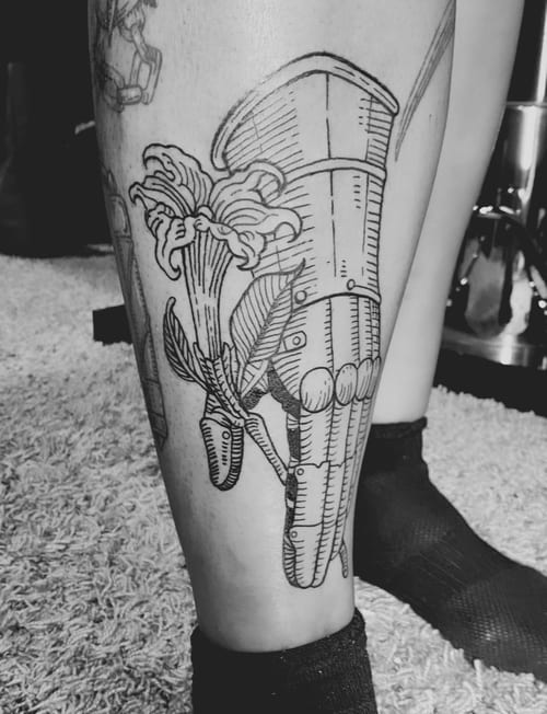 A black and grey linework tattoo on the calf depicting a skeletal hand holding flowers, with bold outlines and detailed shading — by Tag Devilish, los angeles