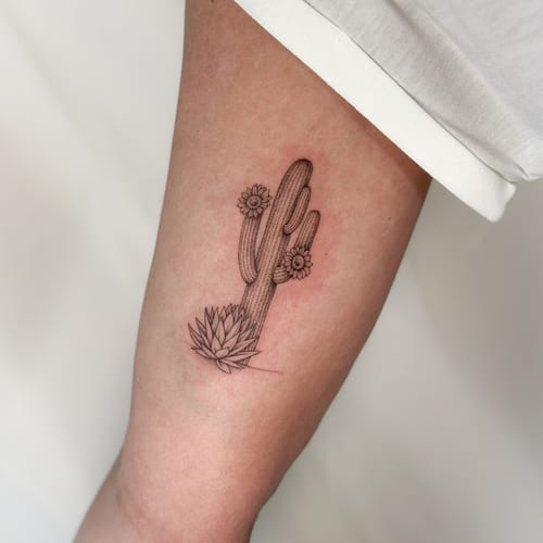 A delicate black and grey fine line tattoo of a cactus with flowers on the thigh — by Melanie Benoit, los angeles
