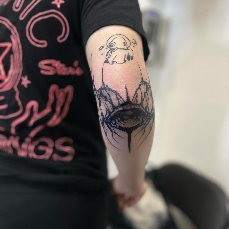 A surreal blackwork tattoo of an eye with a creature on the elbow — by Maddie Ramirez, los angeles