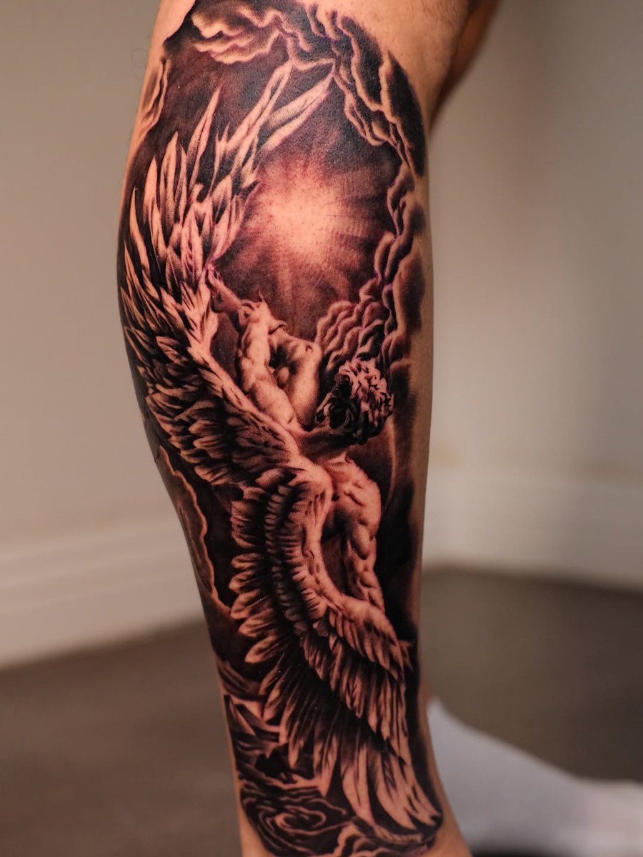 A detailed black and grey tattoo of an angel with wings on the leg, featuring realistic shading and cloud background — by Johnny Ayala, los angeles