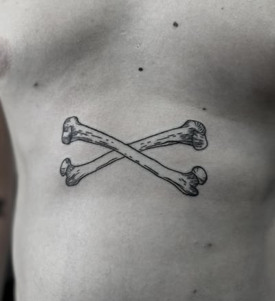 A black and grey crossed bones tattoo on the stomach in blackwork style — by Maddie Ramirez, los angeles
