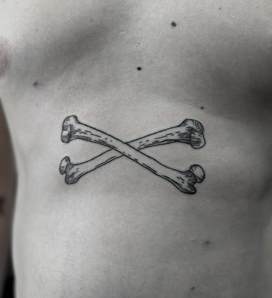 A black and grey crossed bones tattoo on the stomach in blackwork style — by Maddie Ramirez, los angeles