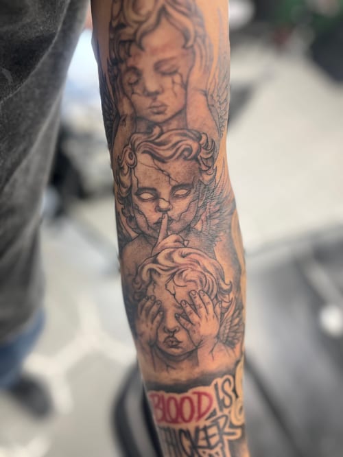 A black and grey realism tattoo on the forearm depicting three angels with detailed shading, accompanied by script text — by Mr._Folks, los angeles