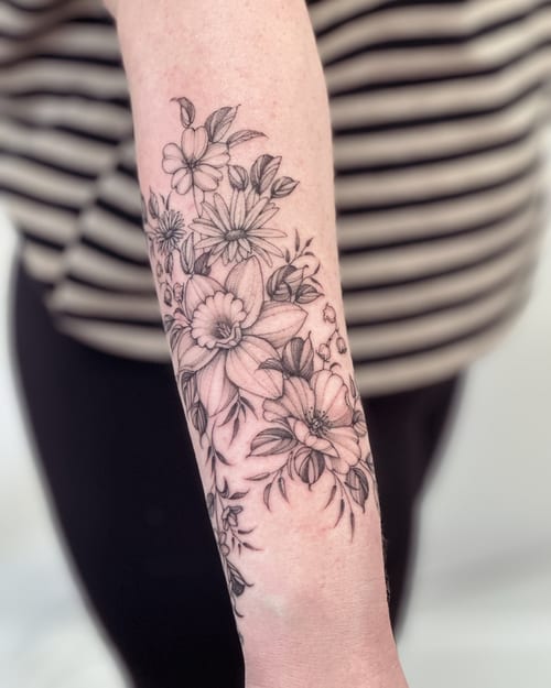 A delicate black and grey floral arrangement tattoo on the forearm, featuring fine line work and clean detailing — by Melanie Benoit, los angeles