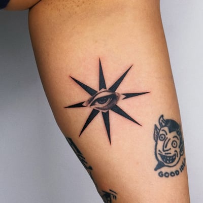 A bold black and grey eye with a starburst design on the thigh, featuring graphic blackwork style — by lunayflorestattoo, los angeles