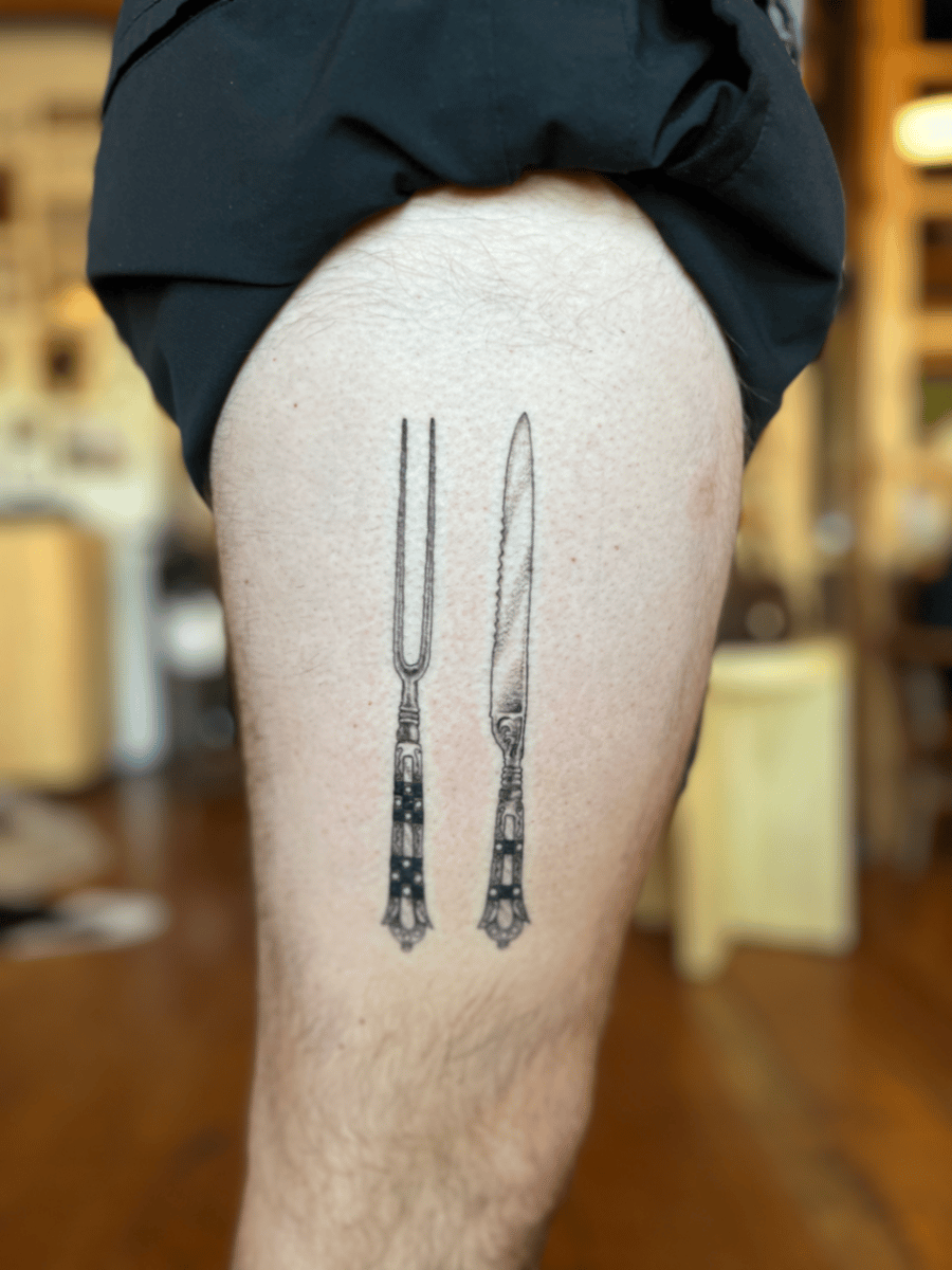 A minimalist black and grey tattoo of a fork and knife on the thigh, featuring clean lines and simple design — by Dylan Aiello, los angeles