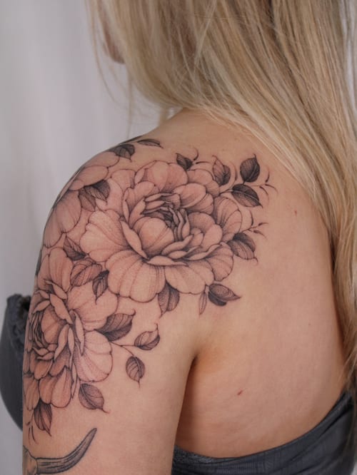 A delicate black and grey floral tattoo on the shoulder featuring detailed flowers and leaves — by Melanie Benoit, los angeles