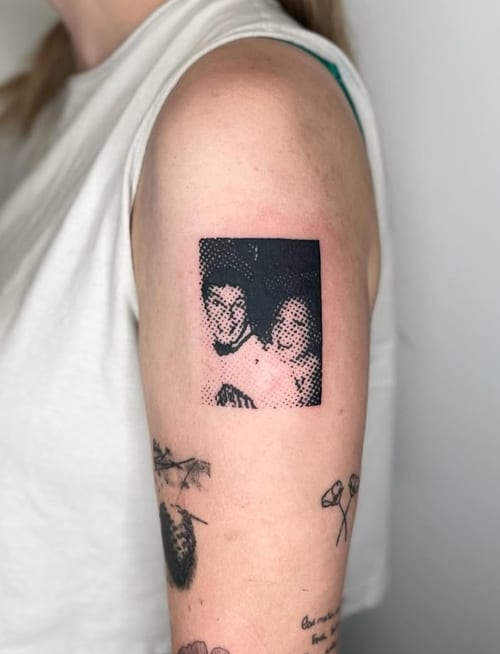 A black and grey dotwork portrait tattoo on the upper arm, featuring two people in a pixelated style — by Level tattoo, los angeles
