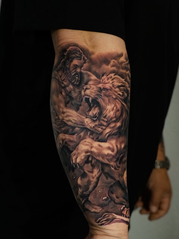 A detailed black and grey tattoo of a man wrestling a lion on the forearm, showcasing realistic shading and dramatic composition — by Johnny Ayala, fontana, ca