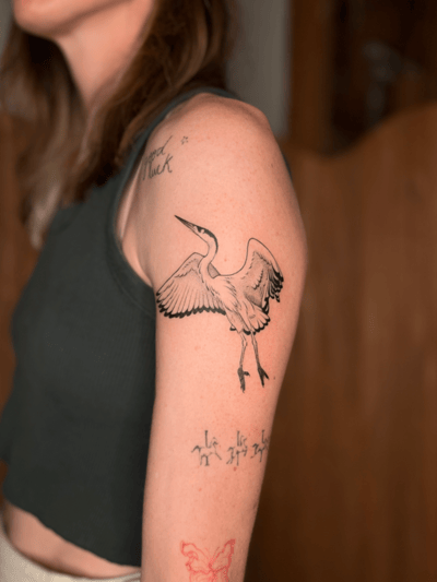 A black and grey linework tattoo of a bird in flight on the upper arm, featuring clean lines and minimal shading — by Dylan Aiello, los angeles