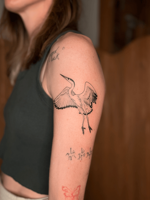 A black and grey linework tattoo of a bird in flight on the upper arm, featuring clean lines and minimal shading — by Dylan Aiello, los angeles