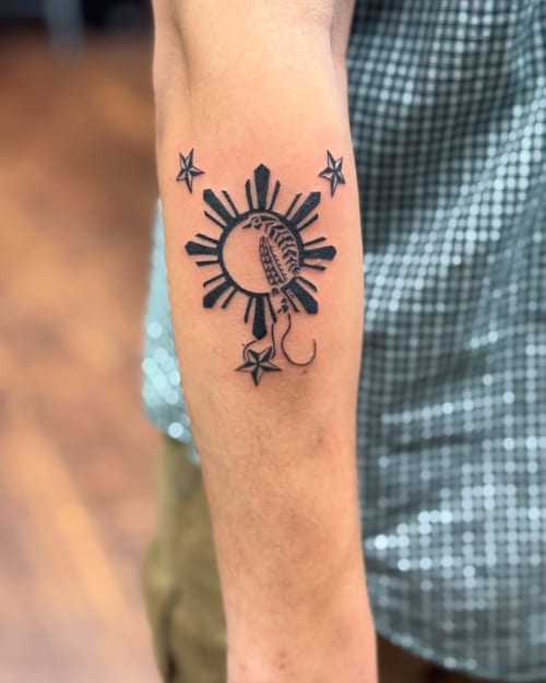 A minimalist black and grey tattoo of a sun and stars with script on the forearm — by Sandra Price, los angeles