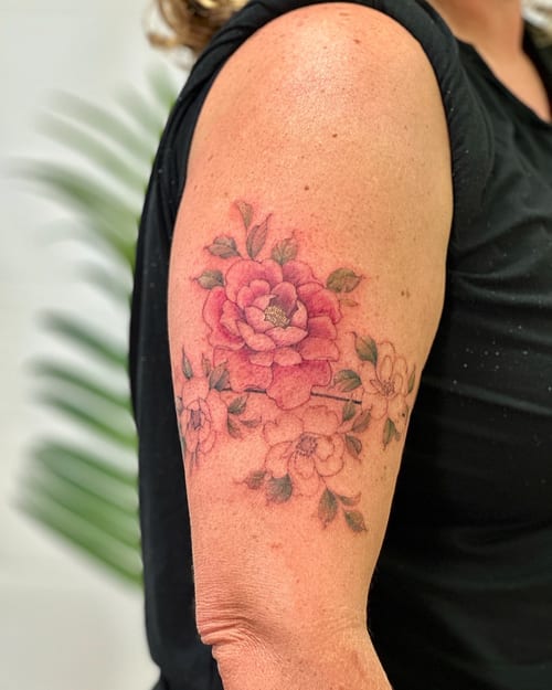 A delicate watercolor flower bouquet tattoo on the upper arm, featuring soft colors and a romantic style — by Melanie Benoit, los angeles