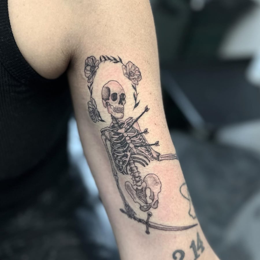 A delicate black and grey skeleton tattoo with floral elements on the arm — by Maddie Ramirez, los angeles