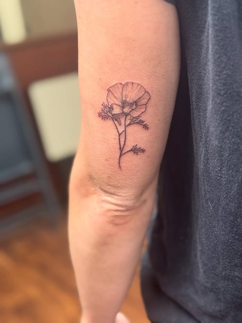 A delicate fine line flower tattoo on the arm, done in black and grey with a minimalist style — by Sandra Price, los angeles