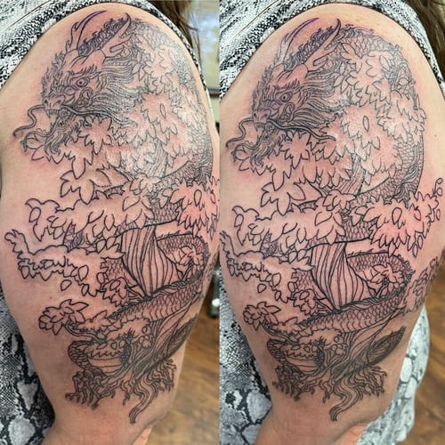 A detailed black and grey linework tattoo of a dragon entwined in a tree on the upper arm, featuring intricate Japanese style elements — by Sandra Price, los angeles