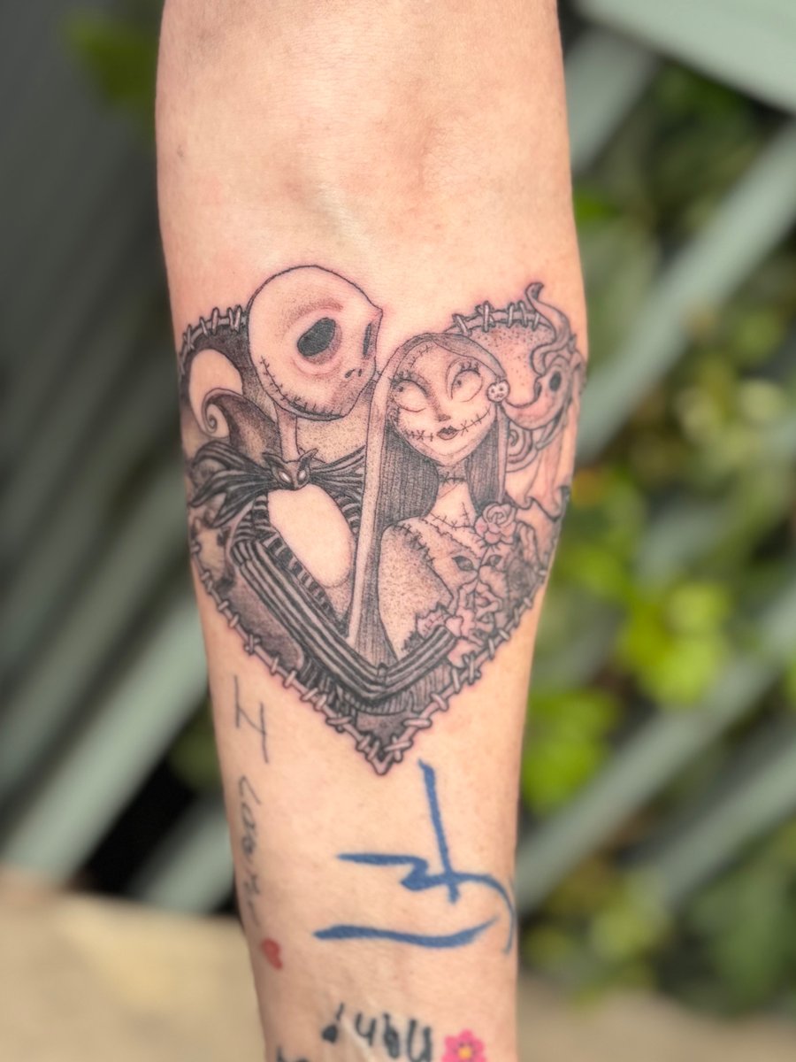 A whimsical black and grey tattoo of characters inside a heart shape on the forearm — by Sandra Price, los angeles