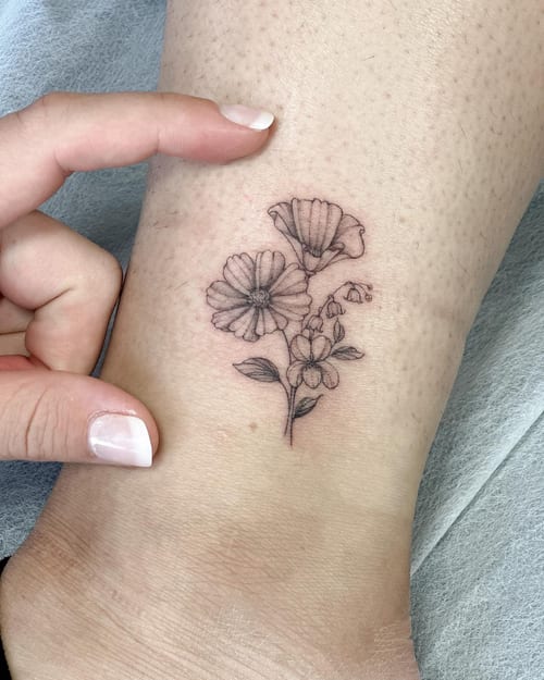A delicate black and grey fine line flower bouquet tattoo on the ankle, featuring a minimalist style — by Melanie Benoit, los angeles