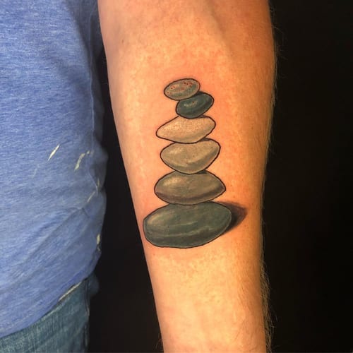 A minimalist and realistic tattoo of stacked stones on the forearm, using a subtle color palette — by Sandra Price, los angeles