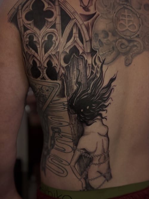 A black and grey back tattoo featuring gothic architecture, a chained woman, and skulls with intricate details — by Maddie Ramirez, los angeles