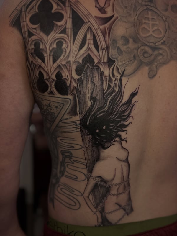 A black and grey back tattoo featuring gothic architecture, a chained woman, and skulls with intricate details — by Maddie Ramirez, palm desert, ca