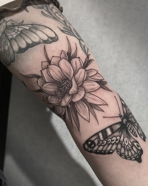 A black and grey tattoo on the forearm featuring a detailed flower and butterfly, rendered in fine line and blackwork style — by Shelby Bianco, los angeles