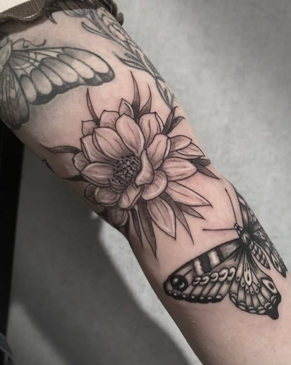 A black and grey tattoo on the forearm featuring a detailed flower and butterfly, rendered in fine line and blackwork style — by Shelby Bianco, ventura, ca