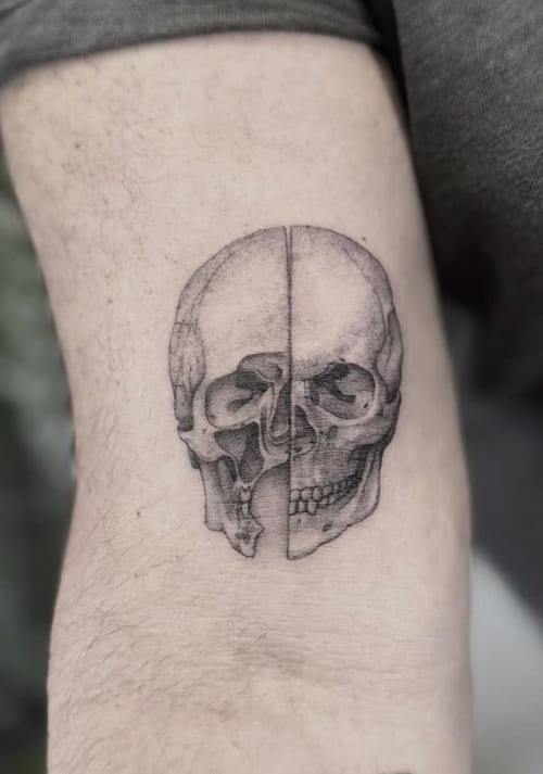 A black and grey realistic skull tattoo on the arm, featuring detailed shading and a split design — by Jian Liang, los angeles