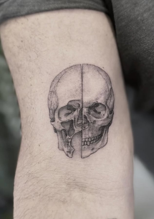 A black and grey realistic skull tattoo on the arm, featuring detailed shading and a split design — by Jian Liang, los angeles
