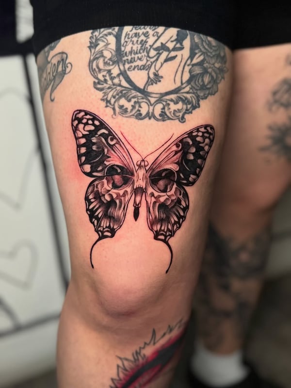 A black and grey butterfly tattoo on the thigh featuring a skull pattern within the wings, done in a graphic blackwork style — by zealous, los angeles