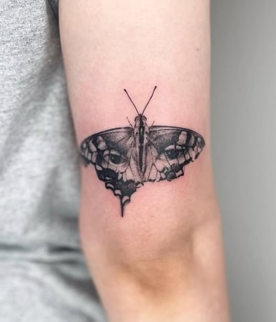 A black and grey tattoo of a butterfly with realistic eyes on its wings, placed on the arm — by Level tattoo, los angeles