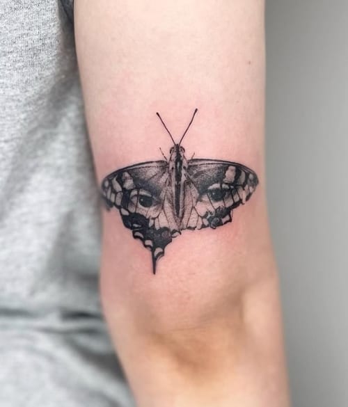 A black and grey tattoo of a butterfly with realistic eyes on its wings, placed on the arm — by Level tattoo, los angeles