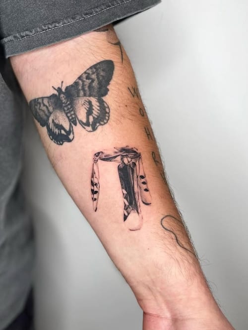 A black and grey illustrative tattoo of a butterfly and a bandana on the forearm, featuring bold lines and shading — by Level tattoo, los angeles