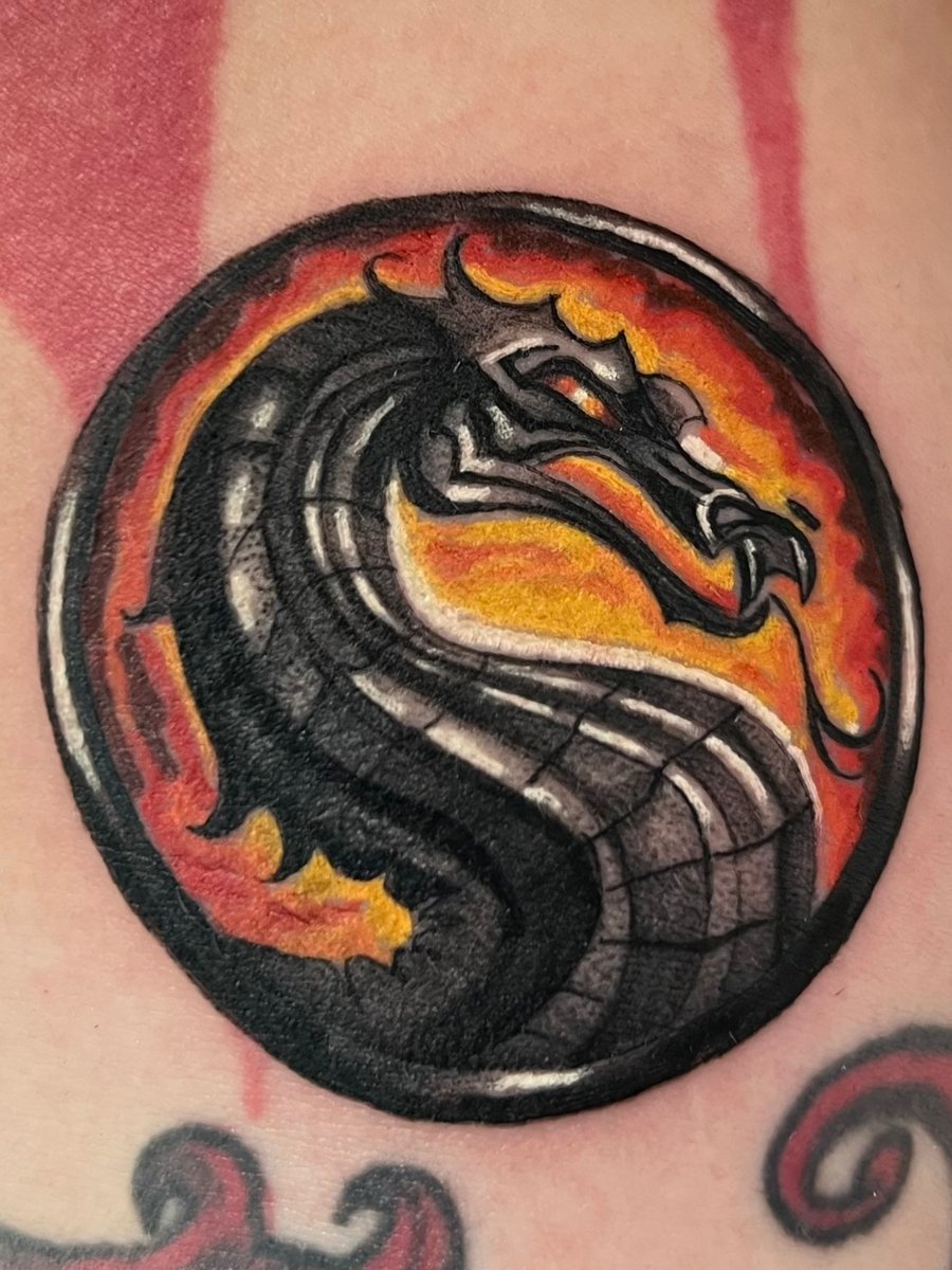 A vibrant neo-traditional dragon head with bold black outlines and fiery orange accents, creating a striking circular design — by Josue Bravo, los angeles