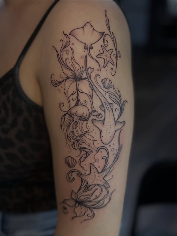 An intricate black linework tattoo of an underwater scene with jellyfish and starfish on the upper arm — by Maddie Ramirez, palm desert, ca