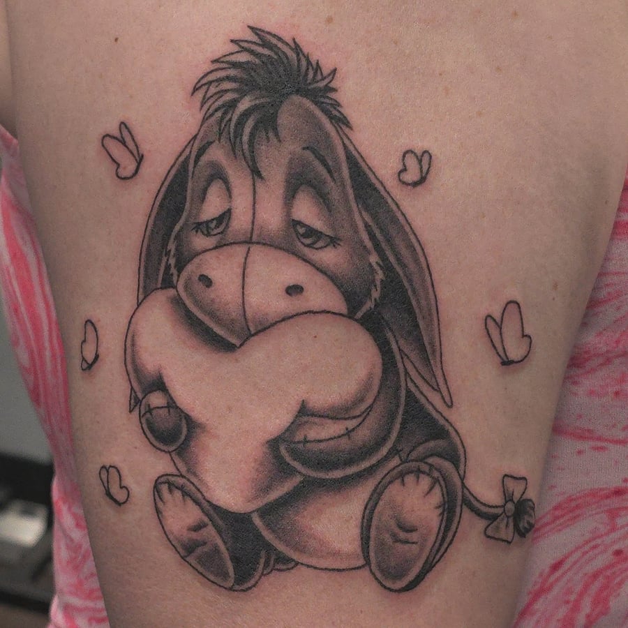 A whimsical black and grey tattoo of a cartoon donkey holding a heart on the upper arm — by Miguel ANGELO, los angeles