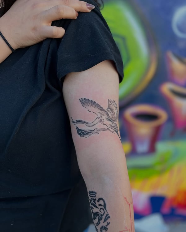 A delicate blackwork tattoo of a flying crane on the upper arm, featuring minimal linework — by Dylan Aiello, los angeles