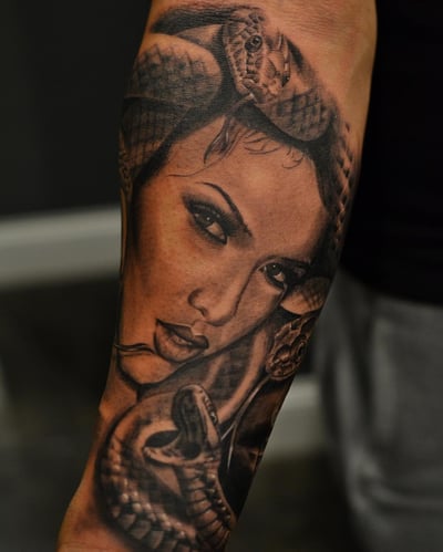A black and grey realistic tattoo of Medusa with snakes on the forearm, showcasing detailed shading and lifelike features — by Johnny Ayala, los angeles