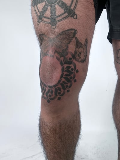 A bold blackwork tattoo on the knee featuring a geometric pattern with a butterfly and cat design — by Brian Kies, los angeles