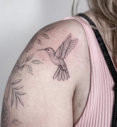 A delicate black and grey fine line hummingbird tattoo on the shoulder, showcasing intricate details and a minimalist style — by Melanie Benoit, los angeles