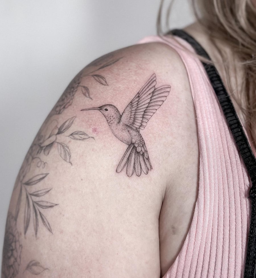 A delicate black and grey fine line hummingbird tattoo on the shoulder, showcasing intricate details and a minimalist style — by Melanie Benoit, los angeles