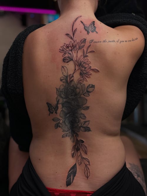 A delicate black and grey floral and butterfly cover-up tattoo on the back — by Maddie Ramirez, los angeles