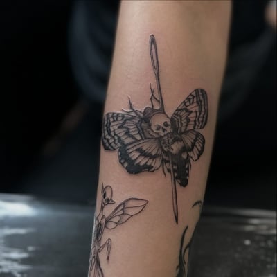 A black and grey tattoo of a moth with a skull and needle on the forearm, done in blackwork and fine line style — by Maddie Ramirez, los angeles