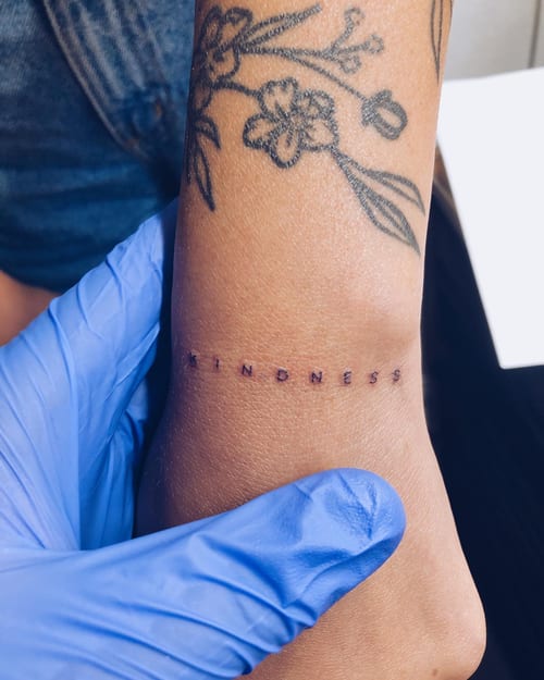 A minimalist black ink script tattoo on the wrist featuring the word 'kindness' in simple lettering — by Level tattoo, los angeles