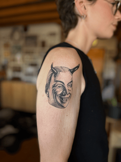 A black and grey portrait of a demonic face with horns on the upper arm, featuring bold lines and shading — by Dylan Aiello, los angeles